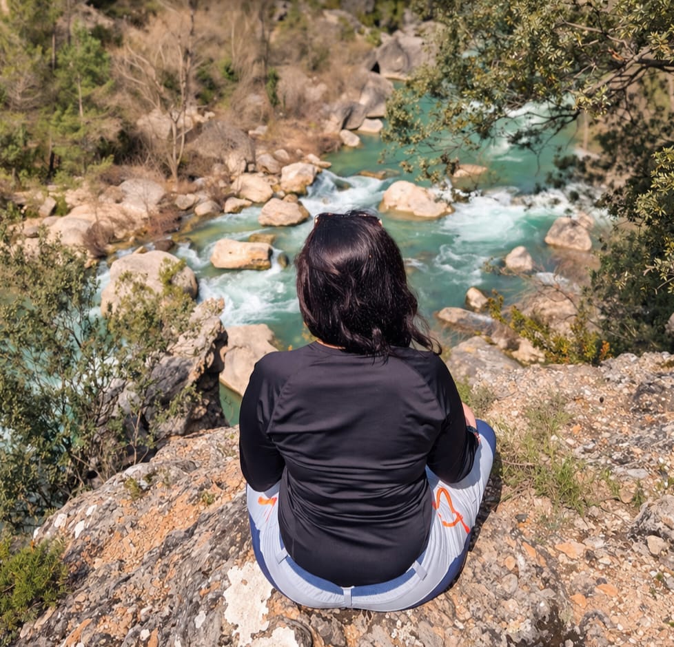 Pilar de espaldas, sentada frente a un río, en un momento de introspección